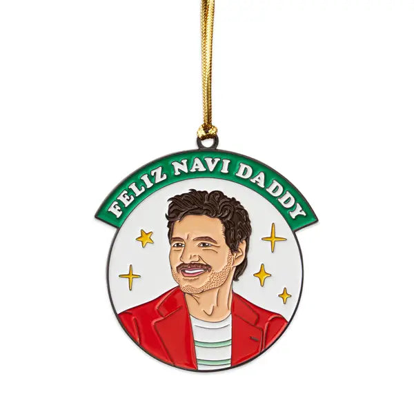 A circular enamel ornament featuring Pedro Pascal with a festive design, wearing a red jacket and green striped shirt. The text "Feliz Navi Daddy" is displayed in green above, with gold star accents in the background. The ornament includes a gold hanging cord.