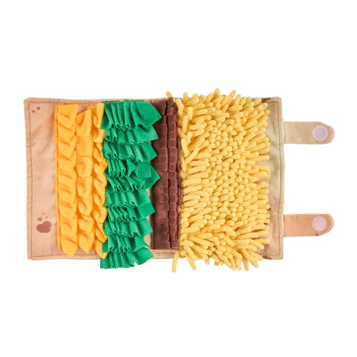 Plush burrito-shaped dog snuffle mat with various textured fabric layers in yellow, green, and brown for hiding treats, featuring an embroidered smiling face when rolled up.