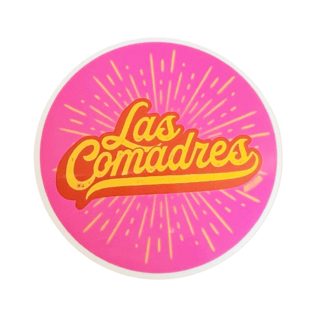 Round pink with the phrase Las Comadres in yellow and red with a yellow burst in the background.