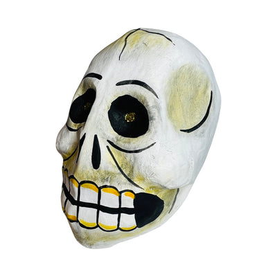Side view of a Paper mache skull with gold glitter eyes and yellow highlights around teeth.