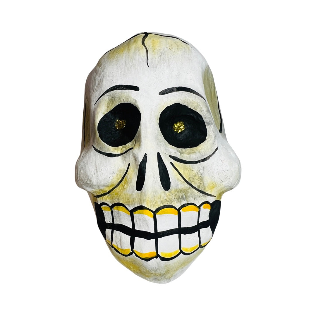 Paper mache skull with gold glitter eyes and yellow highlights around teeth.