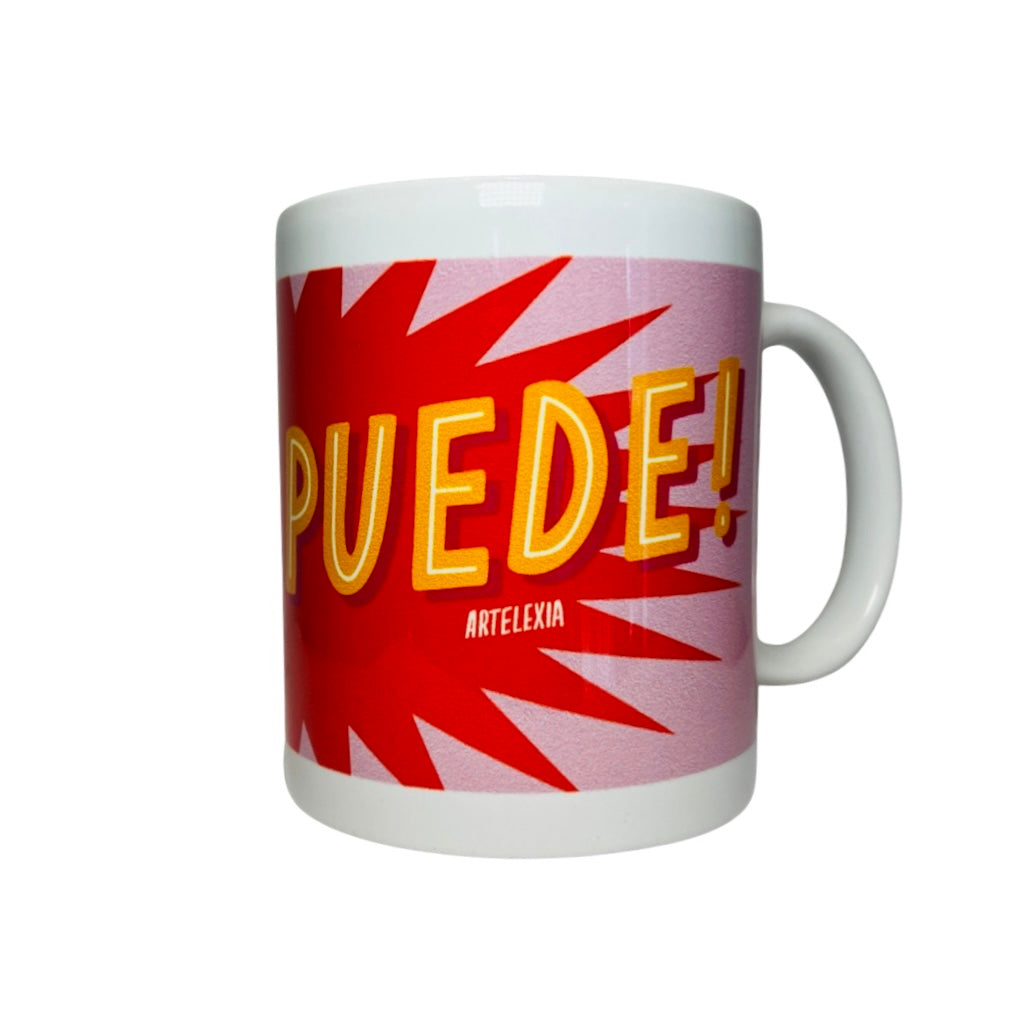 Side view of a White mug with the phrase SI SE PUEDE in orange lettering with a red and pink text bubble background.