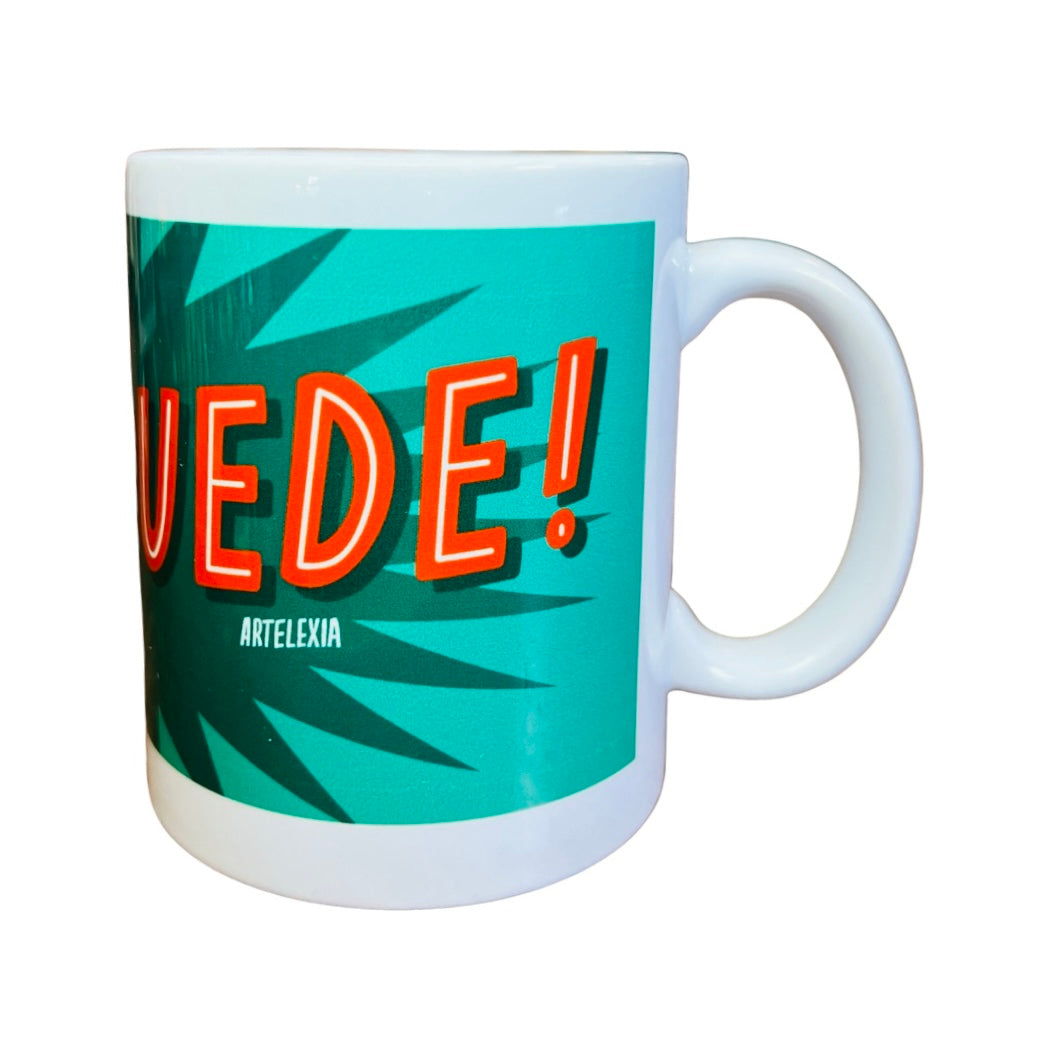 side view of a White mug with the phrase SI SE PUEDE in orange lettering with a Green and dark green text bubble background.