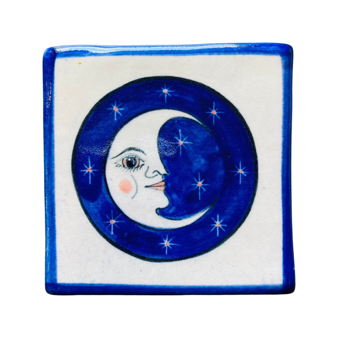 Blue and white square stoneware coaster with an image of the moon with a smiley face