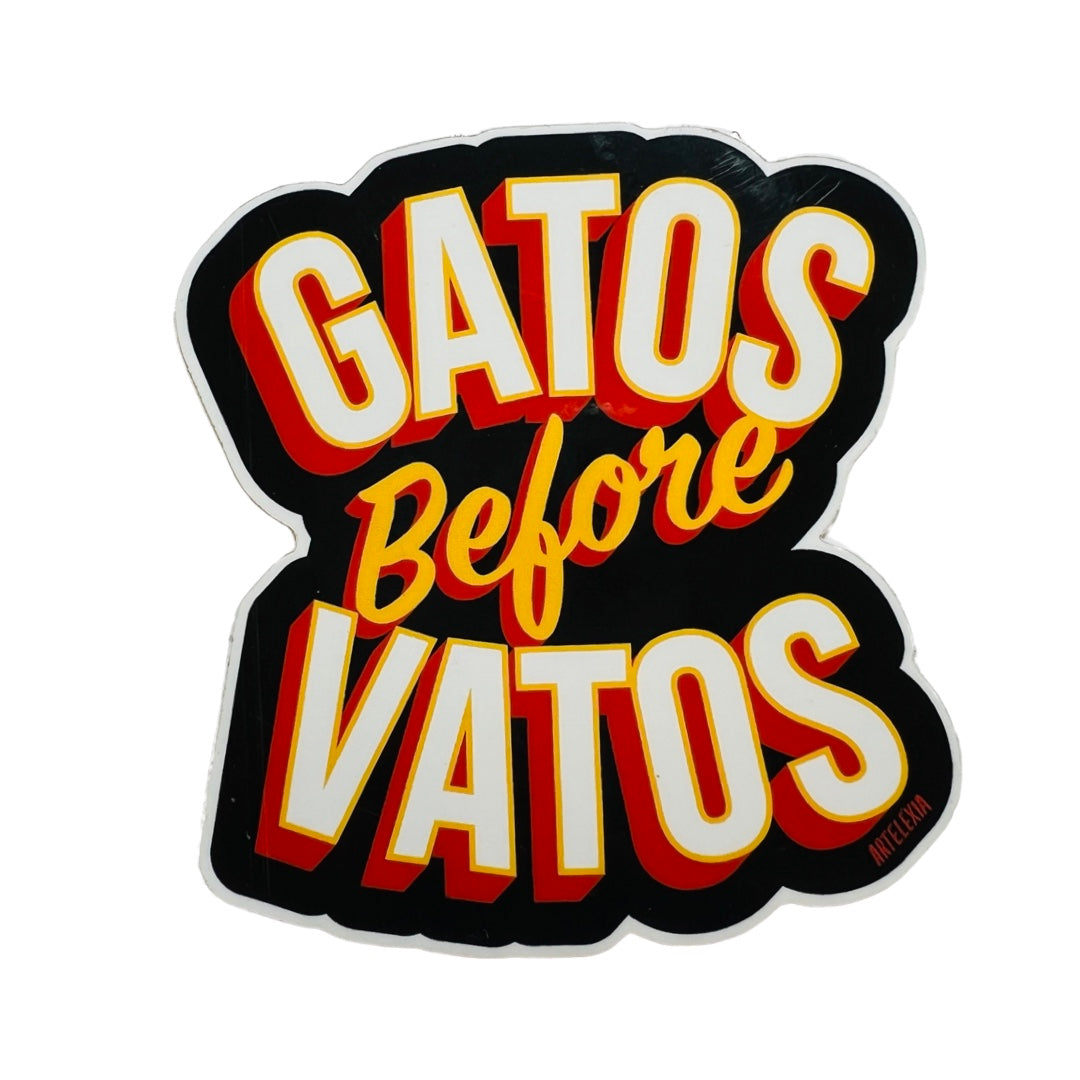 Sticker of the phrase Gatos before Vatos in white lettering outlined in yellow and orange with a black background