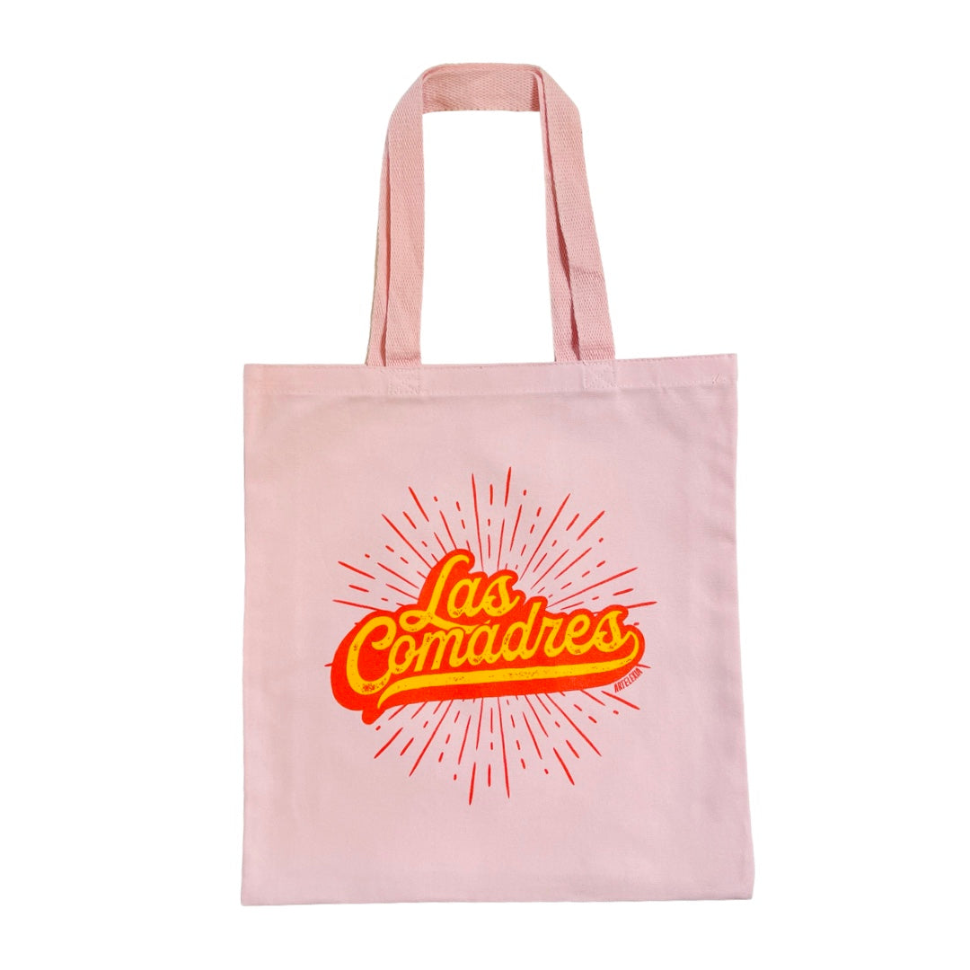 Pink canvas tote bag with the phrase Las Comadres in yellow letting with a red outline and a red burst in the background.