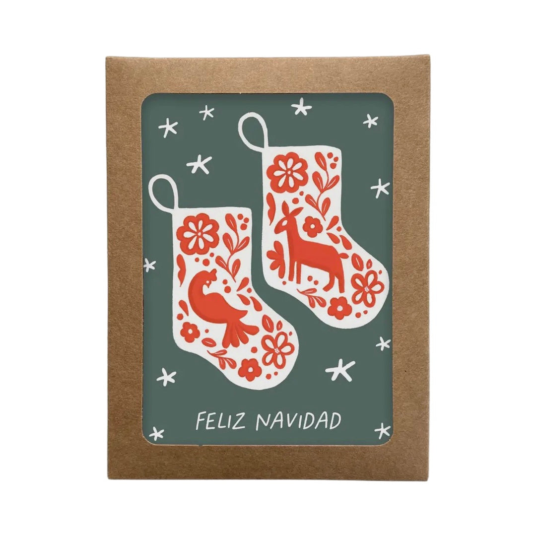 dark sage green card with white stars featuring a set of white stockings with a red otomi design and the phrase Feliz Navidad in white lettering.