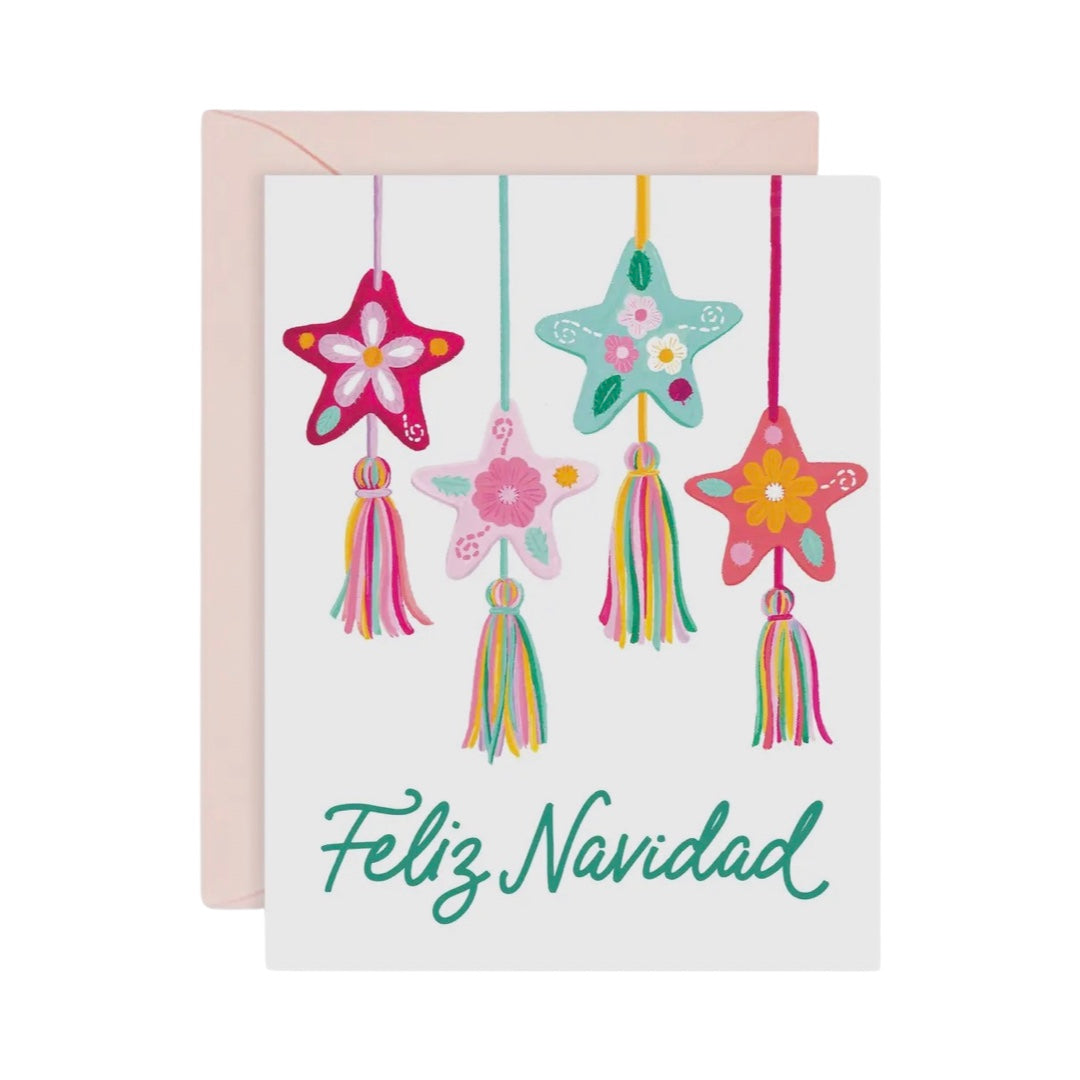 white card featuring illustrations of four felt Mexican star ornaments with a tassel in various pastel colors and the phrase Feliz Navidad in green lettering.