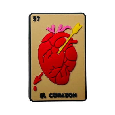 Beige rubber chancla, croc, charm with a red heart and arrow and the phrase El Corazon in black lettering. 