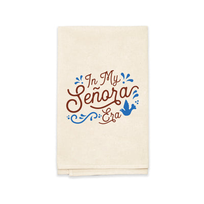 Natural towel with the phrase In My Senora era in brown lettering featuring a blue bird and filagree. towel folded in quarter