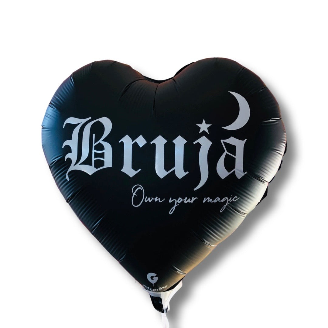 Black heart shaped ballon with the word Bruja in white lettering. Translation: Witch