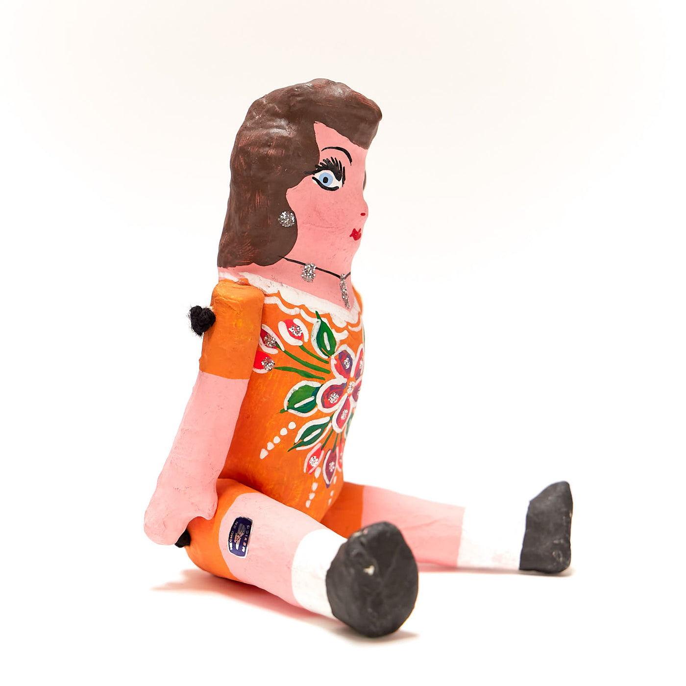 Side view of paper muñeca doll. Doll is wearing a light orange dress.