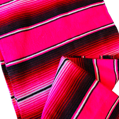 Close up view of a pink serape striped blanket folded in half.