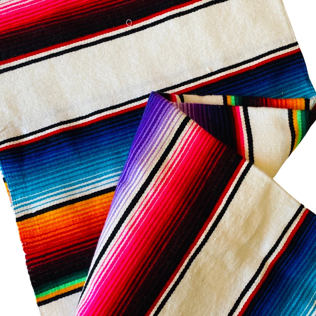 Close up view of a white serape striped blanket folded in half.