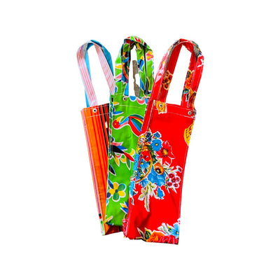 Photo of three variations of the OilCloth wine bottle bag. From left to right: orange with colorful stripes, green with colorful birds and red with flowers.