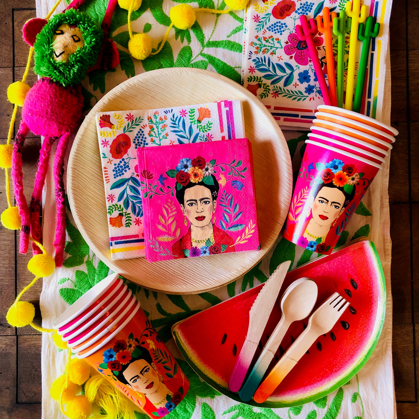top view photograph of our floral paper napkins staged on a tabletop alongside our Frida Kahlo paper cups, disposable paper plates, and our disposable eating utensils