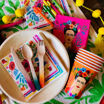 top view photograph of our floral paper napkins staged on a tabletop alongside our Frida Kahlo paper cups, disposable paper plates, and our disposable eating utensils
