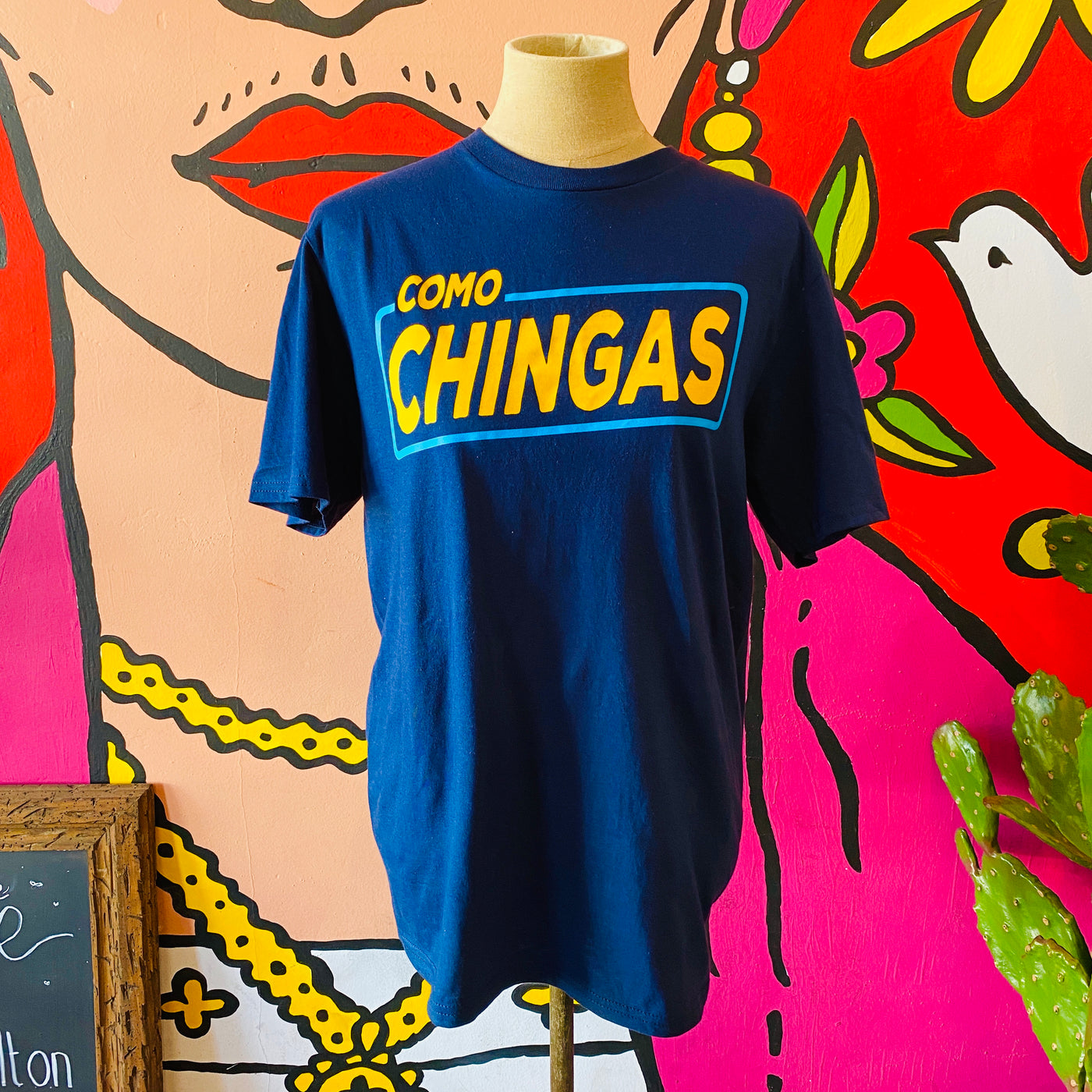 Men's blue, "Como Chingas" phrase t-shirt with yellow detail pictured on mannequin. 
