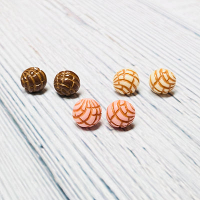 Trio of concha (type of sweet bread) stud earrings in brown, white, and pink.