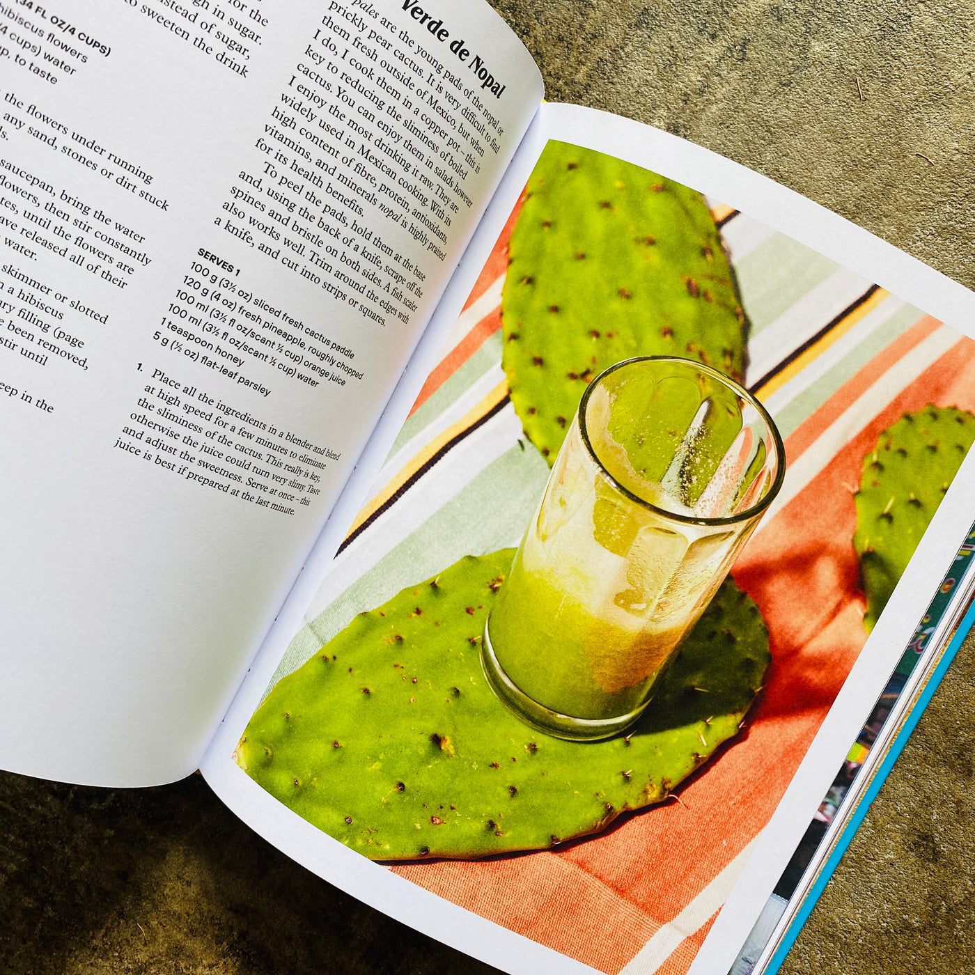 Top view of recipe inside Cuidad De Mexico cookbook. Right side features photo of nopales on a table with a clear glass of green juice. Left side is written out recipe in black and white format.