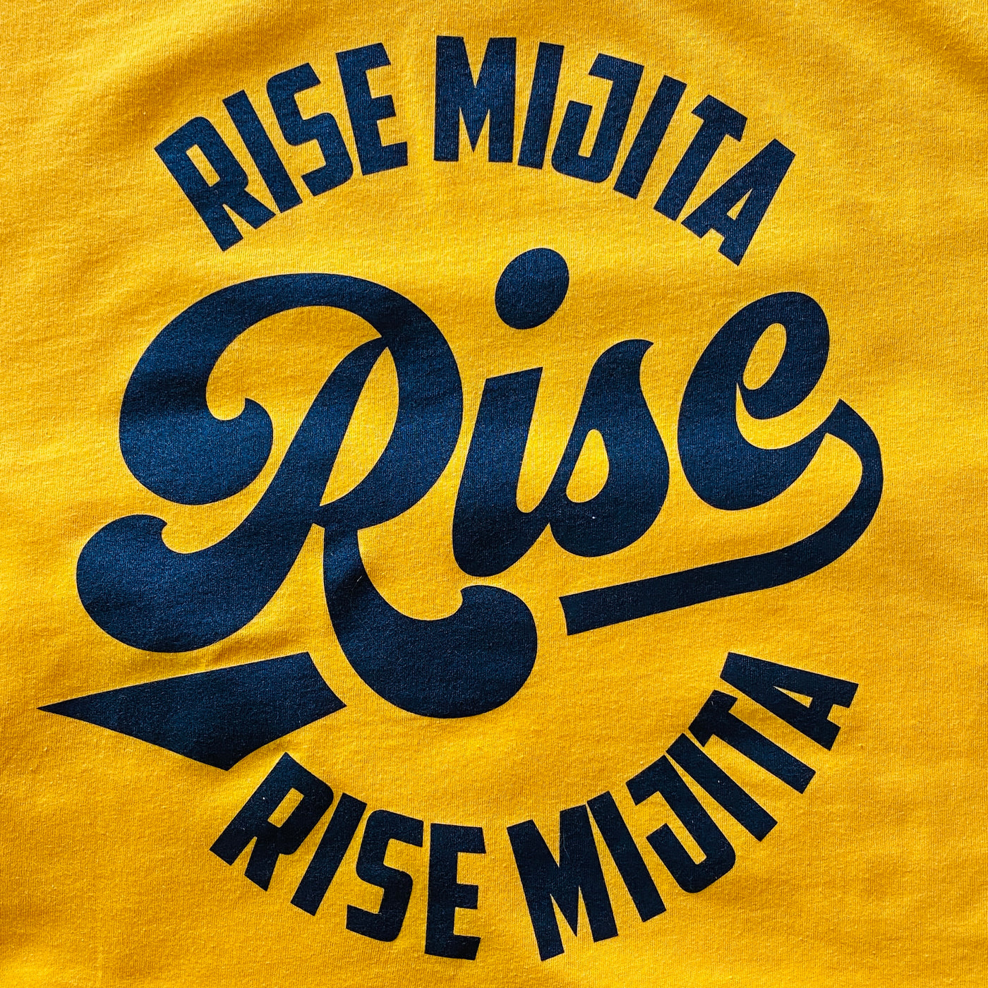 Close up of yellow, "Rise Mijita" phrase t-shirt with black accents.