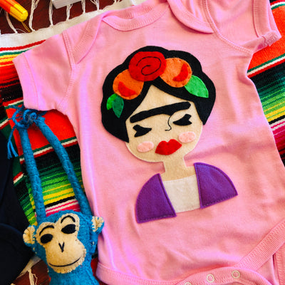 Close up of handmade and hand-stitched Frida Kahlo baby pink onesie.