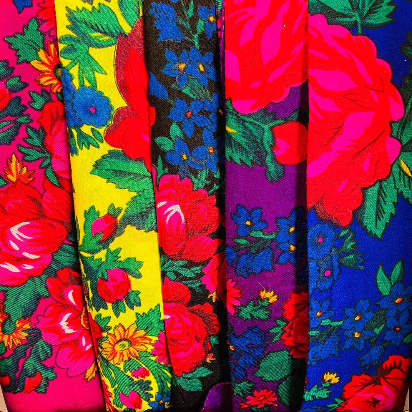 Close up of colorful floral scarves. Colors featured: pink, yellow, black, purple, and blue. 