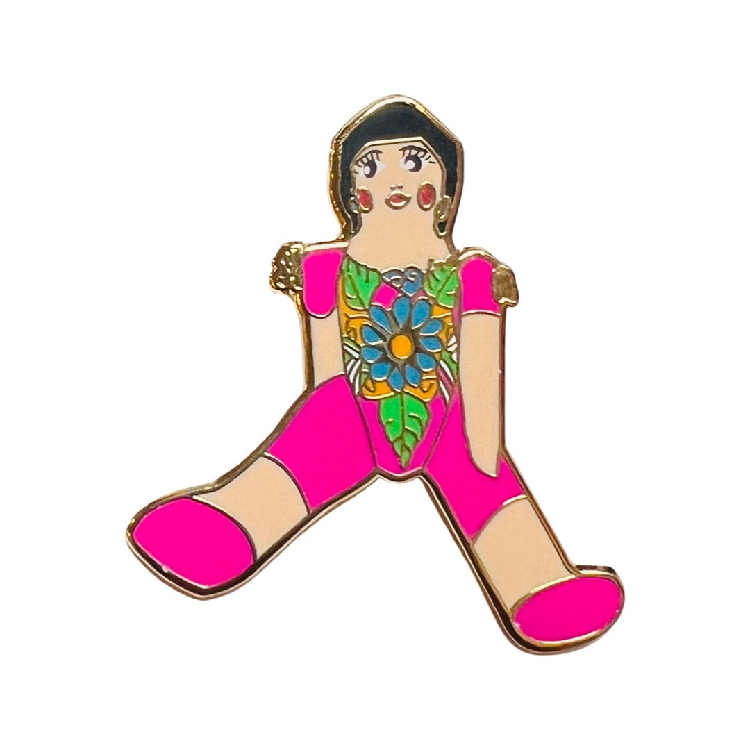 Enamel pin of a traditional Mexican paper mache doll wearing a pink outfit with flowers.
