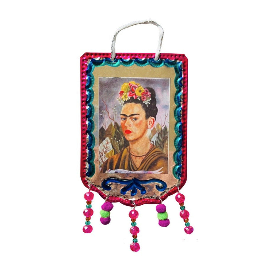 Tin banner with a hand painted border, an image of Frida Kahlo and tassles made of beads and mini pom poms.