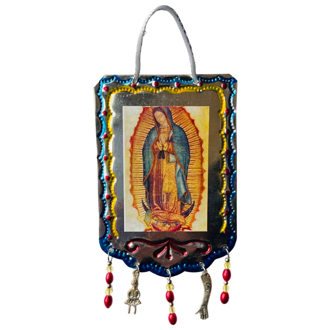 Tin banner with a hand painted border, an image of La Virgen and tassles made of beads and milagro charms.