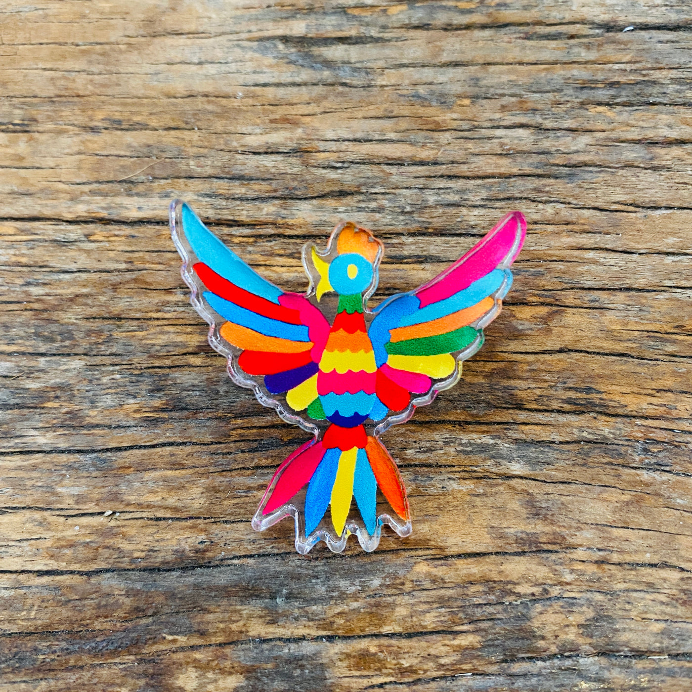 Clear enamel pin with a colorful Otomi bird on it.
