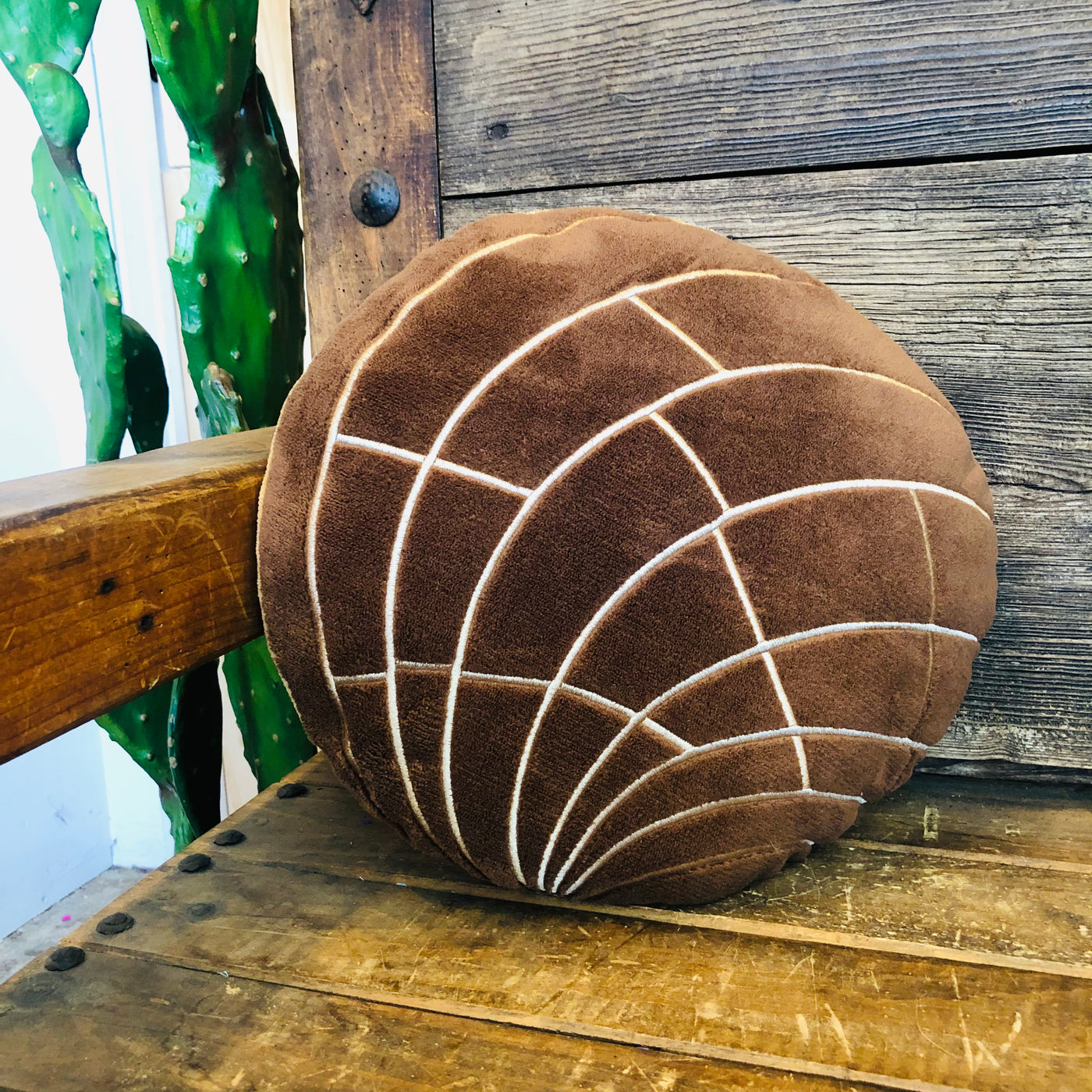 Brown plush concha pillow for the home pictured on wooden chair.