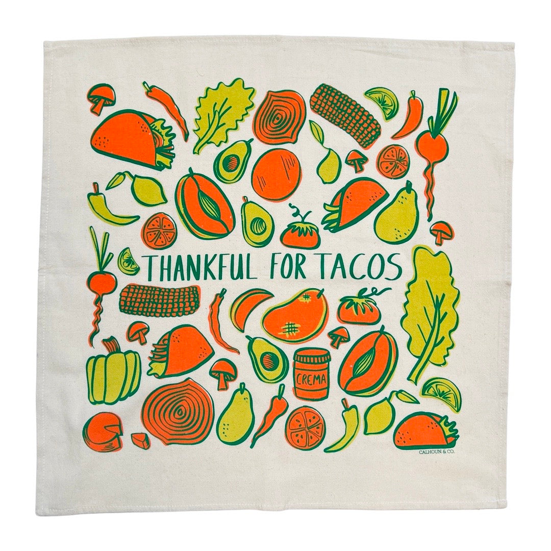 Cotton, "Thankful for Tacos" phrase kitchen towel. Design features different food items with yellow and orange accents. Foods include tacos, chiles, lemons, avocados, onions, and more.