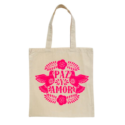 Natural colored tote bag with bright pink design of two doves and the words "Paz y amor" in the center.
