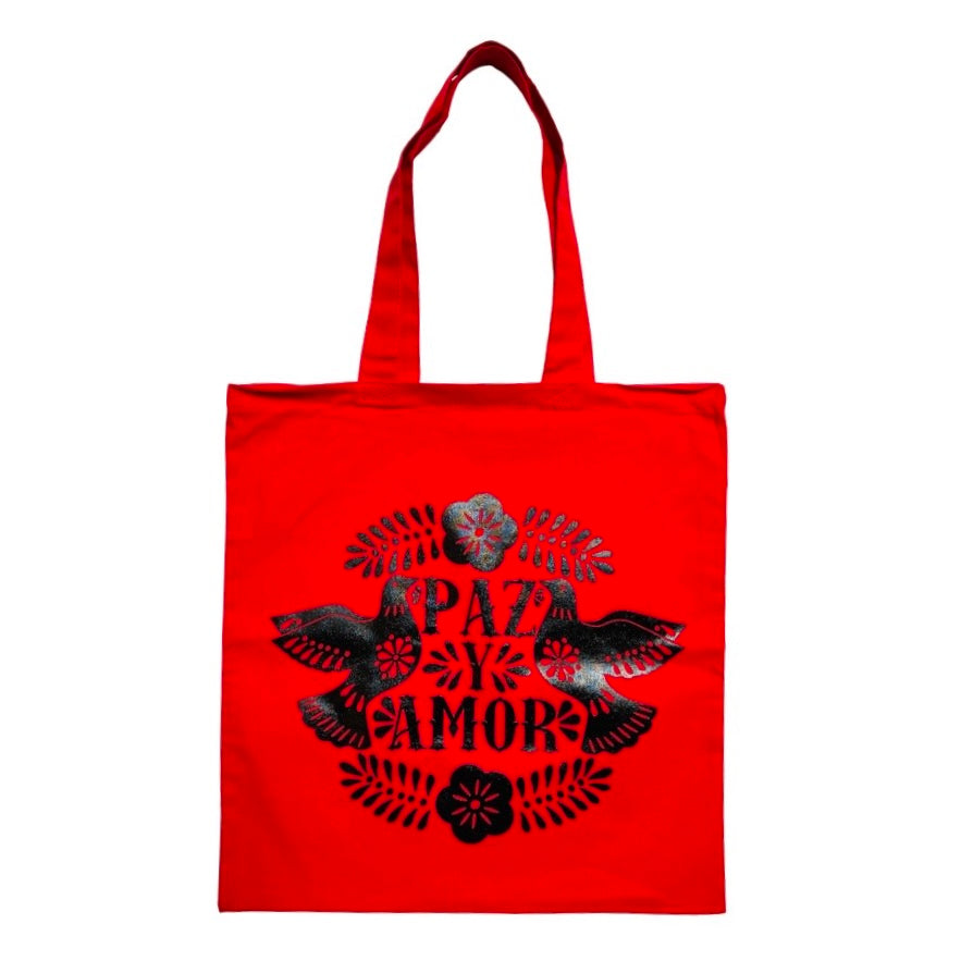 Red tote bag with black design of two doves and the words "Paz y amor" in the center.