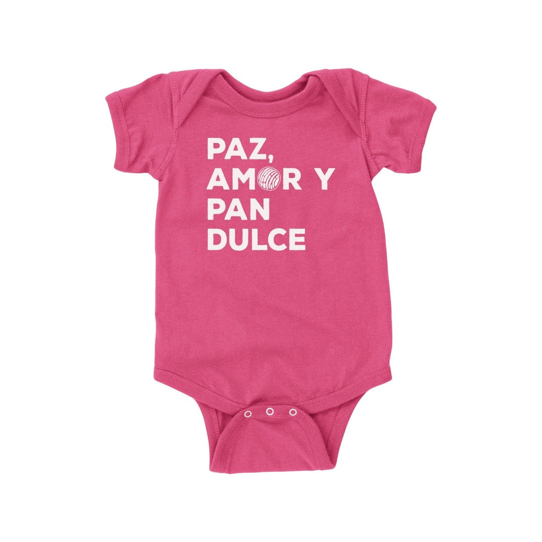 Pink onesie with the phrase Paz, Amor y Pan Dulce in white lettering. Amor has a Mexican concha in place of the "O." Translation: Peace, Love and Pastries.