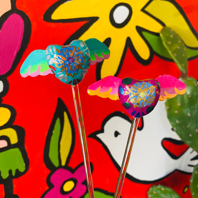 Brightly colorful heart with wings glass stir sticks. Design features flowers in the middle of the heart. Glass stir sticks pictured in front of Artelexia Frida mural.