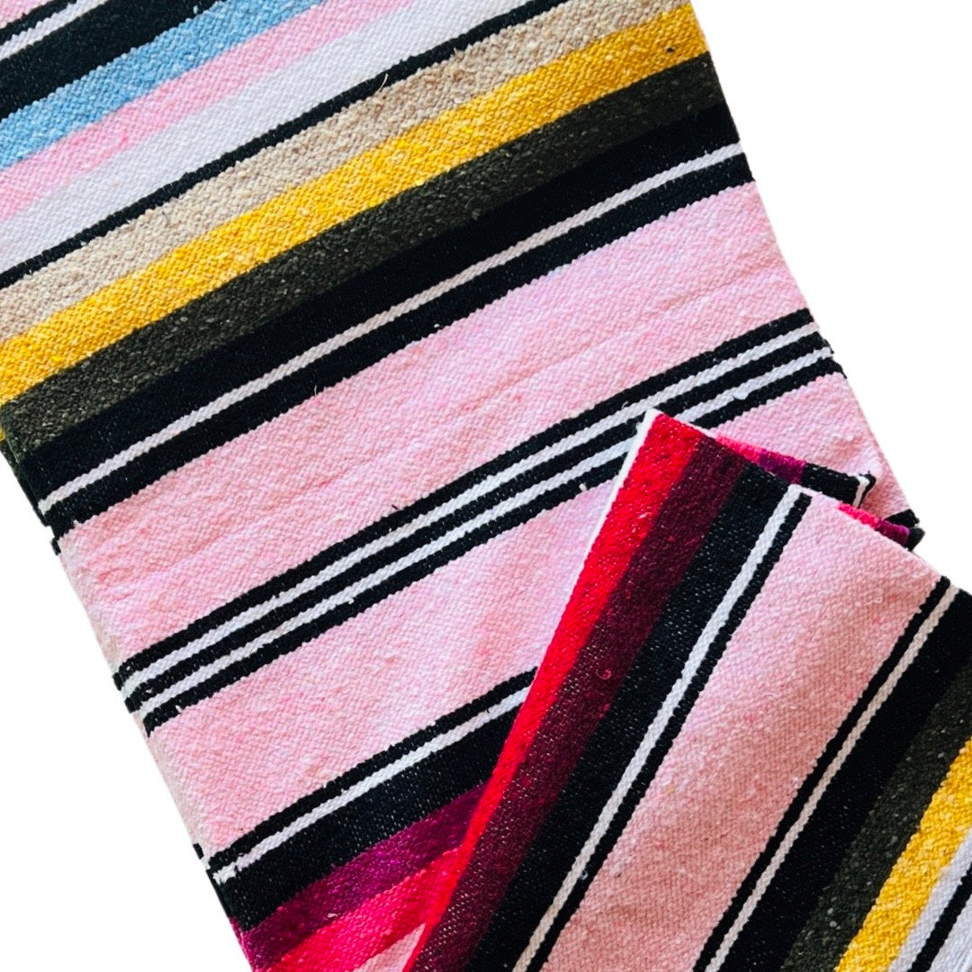 Close up view of light Pink serape striped blanket folded in half.