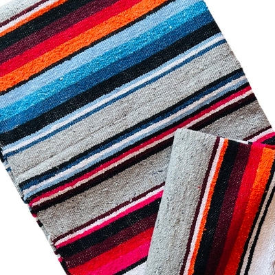 Close up view of a light grey serape striped blanket folded in half.