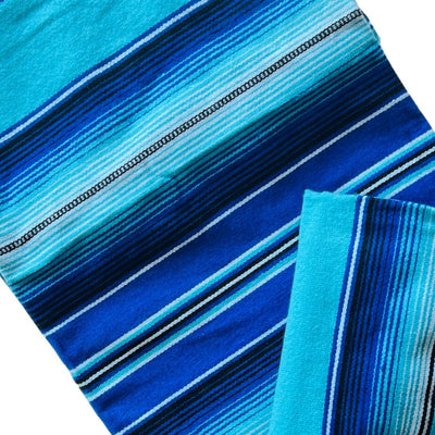 Close up view of a blue and teal serape striped blanket folded in half.