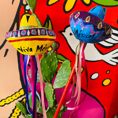 Sombrero paper mache shakers with colorful ribbons pictured in front of the Artelexia Frida mural. 
