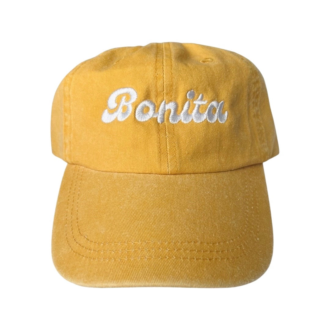 Mustard canvas hat with the phrase Bonita in white embroidered lettering.