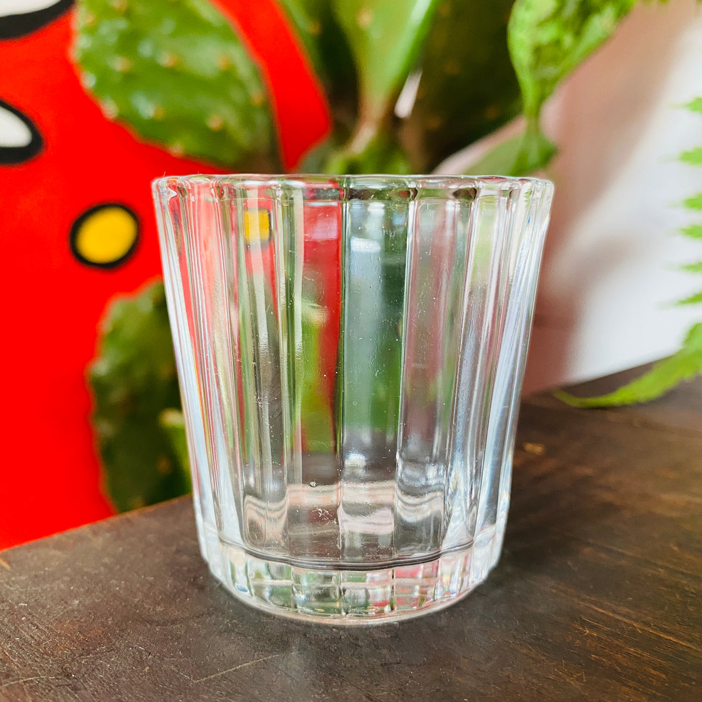 Clear scalloped shot glass pictured on dark wooden table with cactus in the background.