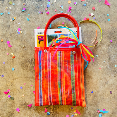 Top view of Frida Loteria pack inside colorful mercado bag. Item pictured on floor with confetti.