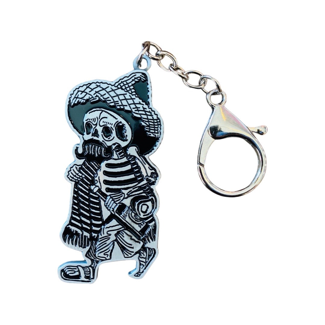 Enamel keychain of a calavera with a mustache, sombrero and bottle of liquor.