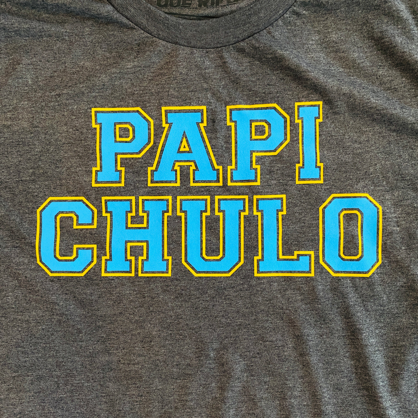 Close up men's gray, "Papi Chulo" phrase t-shirt with blue and yellow detail.