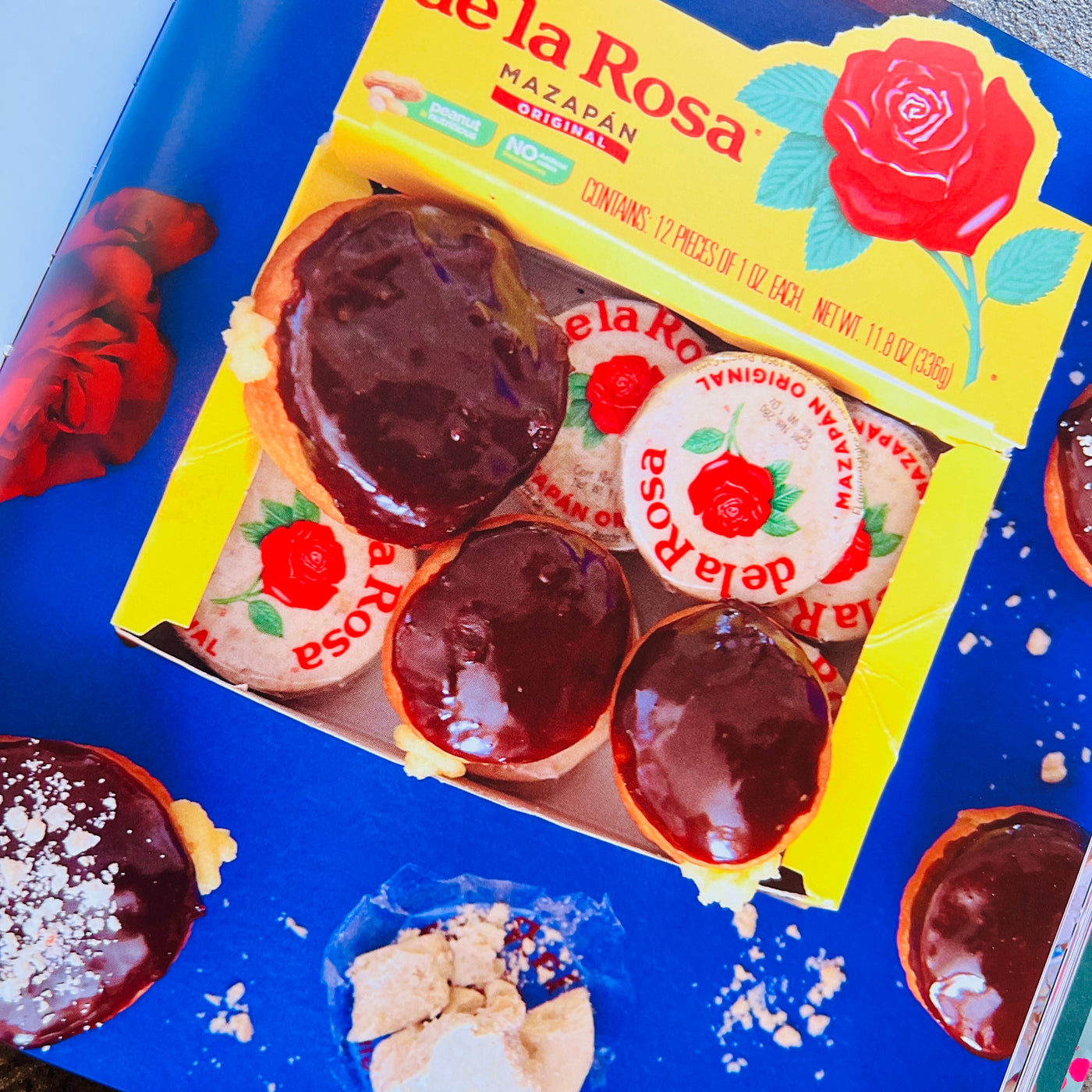 On a blue background is a yellow box of De La Rosa mazapan along with chocolate covered donuts. 