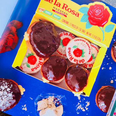 On a blue background is a yellow box of De La Rosa mazapan along with chocolate covered donuts. 