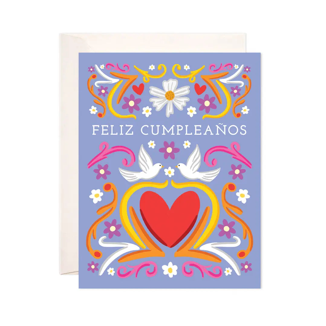 Purple greeting card with two white doves, a red heart and pink, purple and white flowers. Features the phrase Feliz Cumpleaños in white lettering.