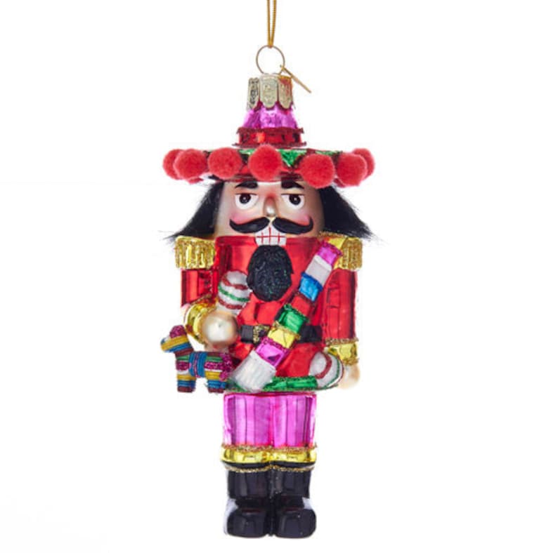 glass mexican nutcracker ornament featuring fake black hair, traditional big teeth, pom pom on hat and a mini pinata 